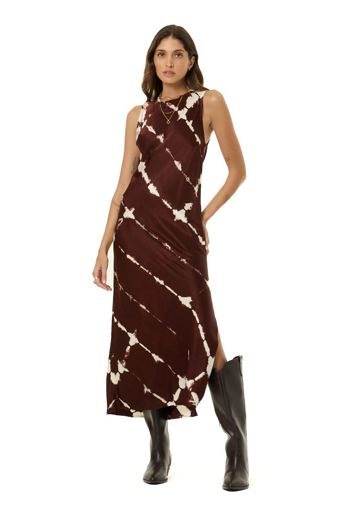 A woman modeling a sleeveless, high-neck, midi dress with a dark brown base and a white tie-dye pattern, paired with brown boots, against a solid white background.