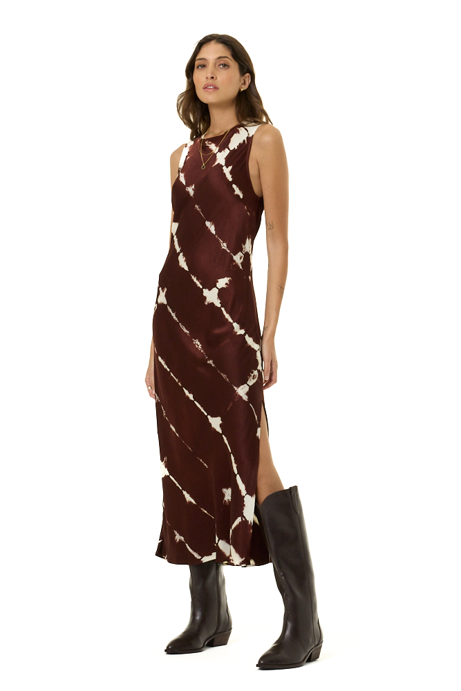 A woman modeling a sleeveless, high-neck midi dress with a diagonal tie-dye pattern in dark burgundy and cream, paired with brown knee-high leather boots, against a solid white background.