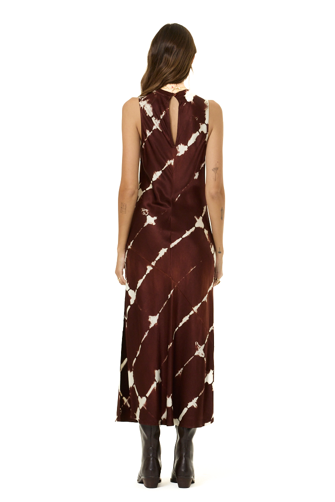 A woman viewed from the back wearing a sleeveless dark brown midi dress with a white tie-dye pattern and a keyhole back, paired with brown boots, on a solid white background.