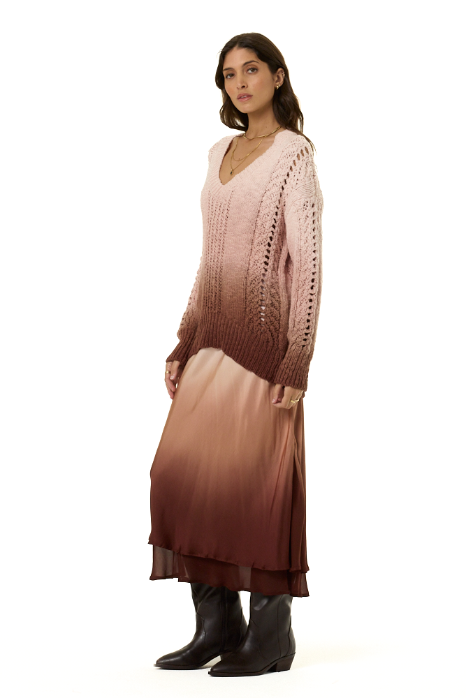 A woman modeling a long-sleeve knit sweater and matching midi skirt set in a dusty pink and brown ombre gradient, paired with black knee-high boots, against a plain white background.