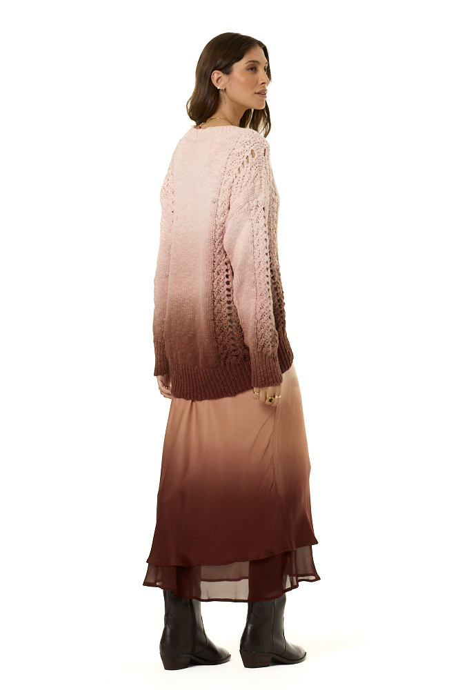 A woman shown from the back wearing a long-sleeve knit sweater and matching midi skirt with an ombré color gradient from light pink at the top to deep burgundy at the bottom, paired with black ankle boots, against a plain white background.