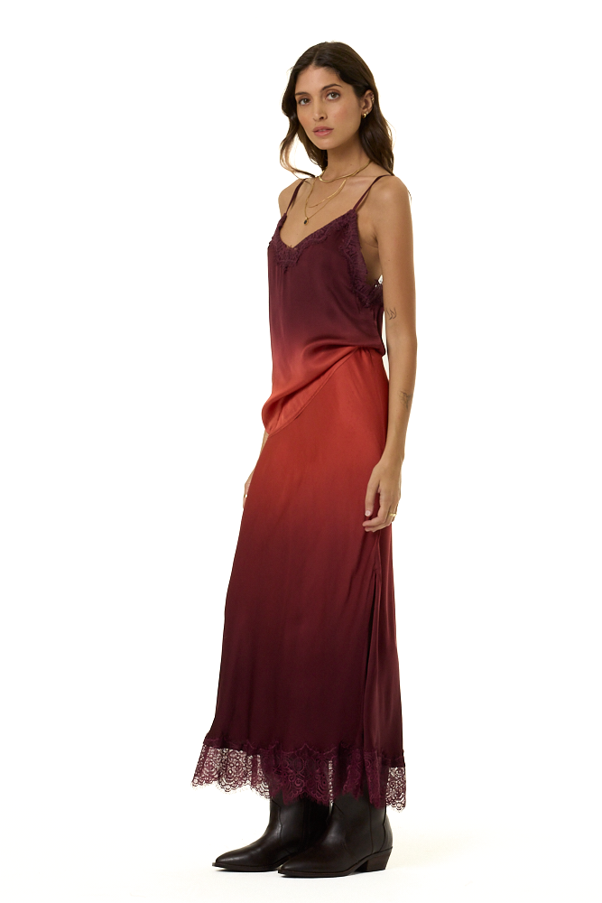 A woman modeling a long satin slip cami and skirt set with a vertical ombré color transition from deep burgundy to rust red, featuring lace trim at the neckline and hem, paired with black ankle boots against a plain white background.