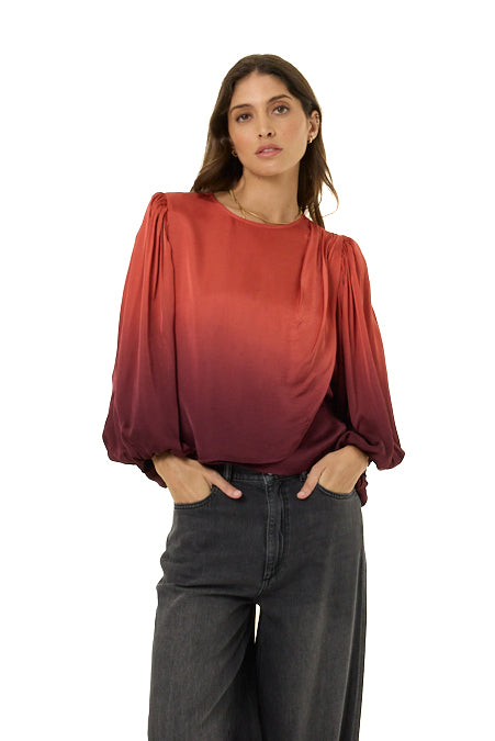 A woman modeling a long-sleeve satin blouse with a vertical red-to-burgundy gradient and voluminous puff sleeves, paired with dark gray wide-leg jeans against a plain white background.