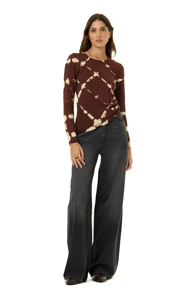 A woman modeling a long-sleeve knit top with a brown and cream tie-dye pattern, paired with dark gray wide-leg pants, against a plain white background.