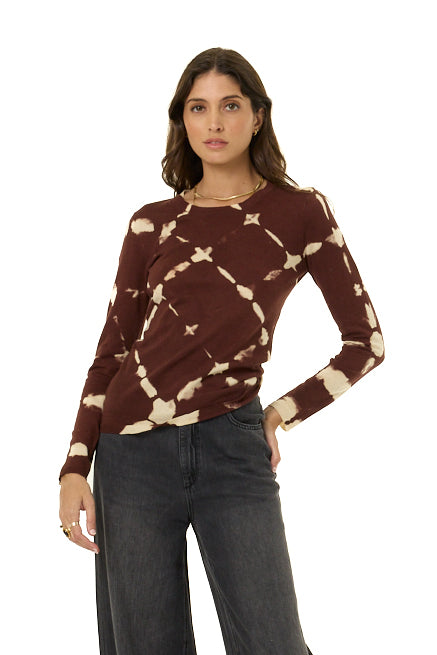 A woman modeling a long-sleeve knit top with a brown and cream tie-dye pattern, paired with dark gray jeans, against a solid white background.