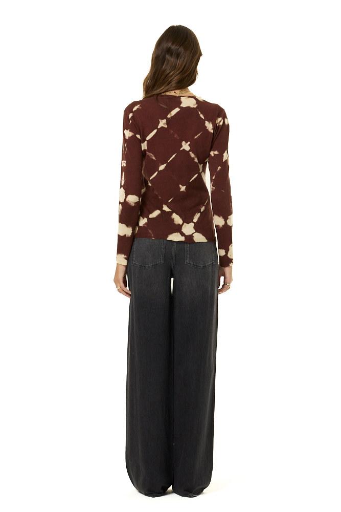 A woman viewed from the back wearing a long-sleeve knit top with a brown and beige tie-dye diamond pattern, paired with wide-leg black pants, against a plain white background.