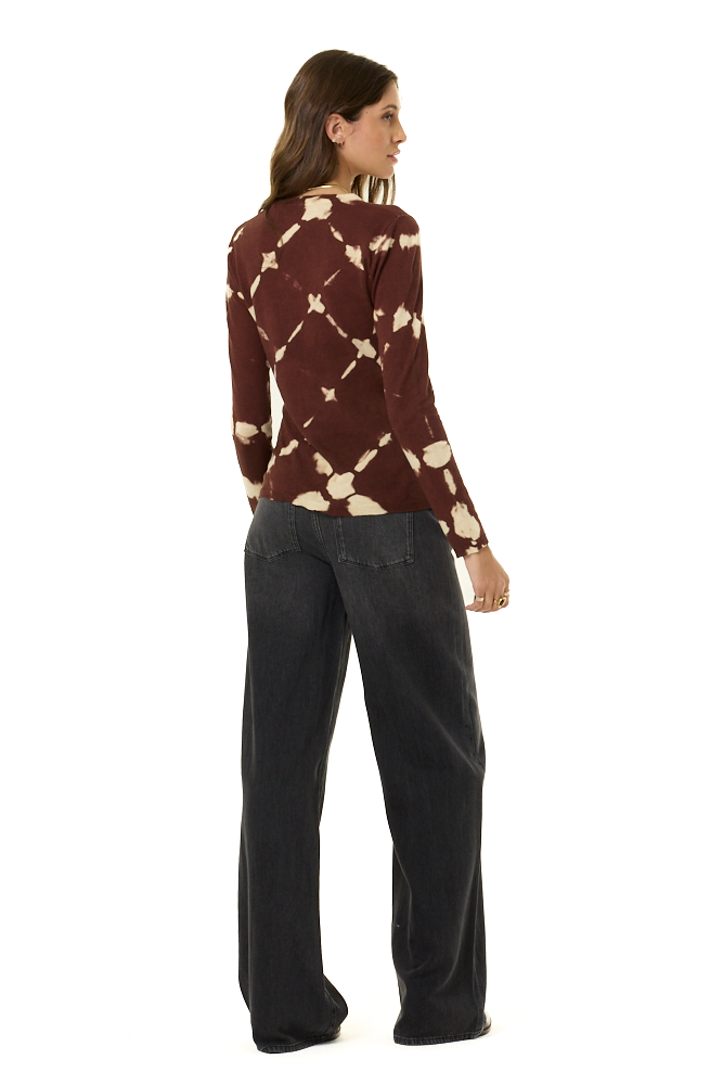 A woman is shown from the back wearing a long-sleeve maroon top with a cream tie-dye pattern and dark charcoal wide-leg pants, set against a plain white background.