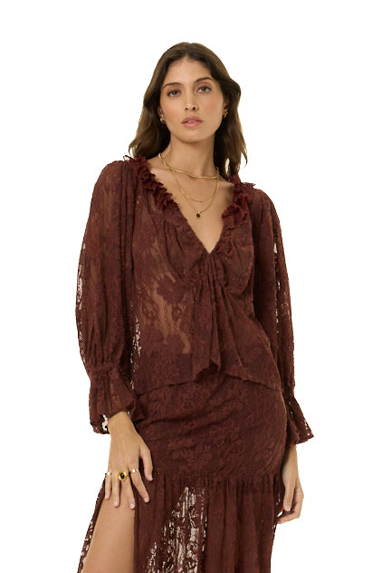 A woman modeling a dark brown lace two-piece set consisting of a long-sleeve ruffled blouse and a matching high-slit skirt, set against a plain white background.