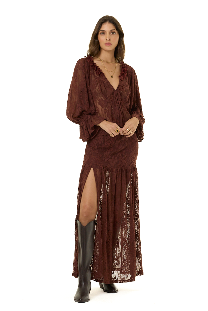 A woman modeling a dark brown lace two-piece set consisting of a long-sleeve ruffled blouse and a matching high-slit skirt, set against a plain white background.