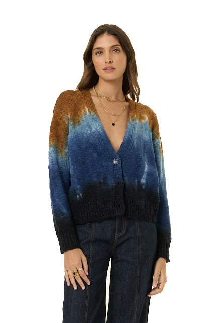 A woman modeling a long-sleeve knit cardigan with a tie-dye style gradient transitioning from brown at the shoulders, through deep blue, to black at the hem and cuffs, paired with dark jeans against a plain white background.