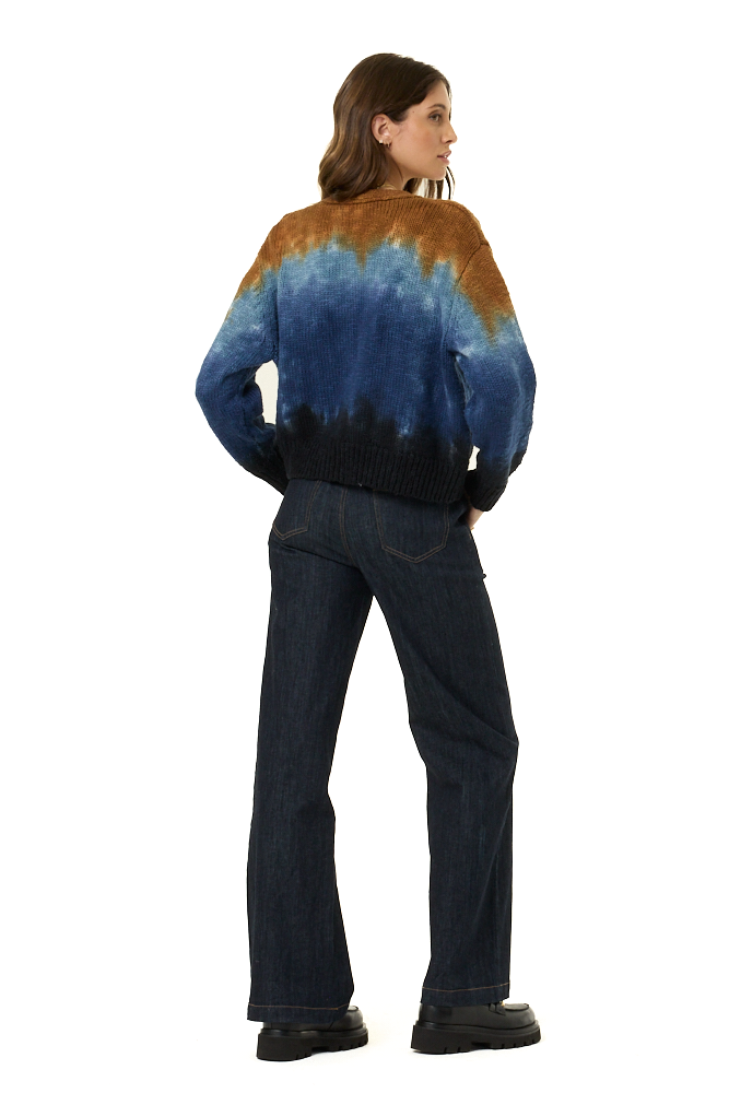 A woman shown from the back wearing a knit sweater with a blue and brown tie-dye pattern and dark blue jeans, photographed against a plain white background.