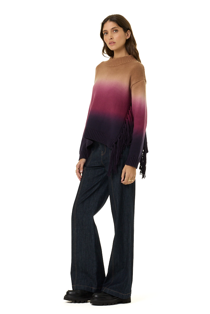 A woman modeling a long-sleeve knit sweater with a brown-to-purple ombré gradient and fringe detailing, paired with dark wide-leg jeans and black shoes, against a plain white background.