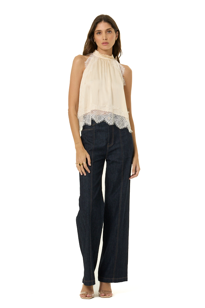 A woman modeling a sleeveless cream top with a lace hem and dark wide-leg jeans against a plain white background.
