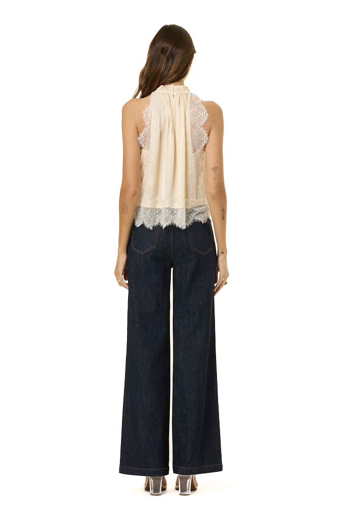 A woman shown from the back wearing a cream sleeveless top with lace trim and dark wide-leg jeans, photographed against a plain white background.