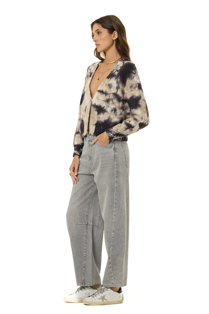 A woman modeling a long-sleeve button-up shirt with a black and beige tie-dye pattern, paired with wide-leg light gray jeans and white sneakers, shown against a plain white background.