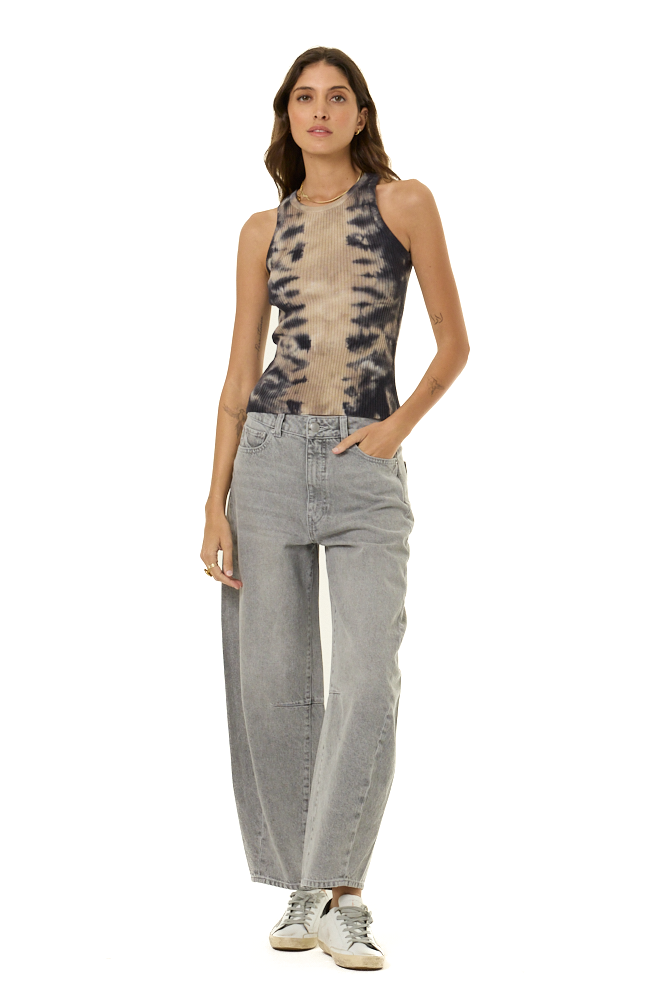 A model stands against a white background wearing a sleeveless tie-dye top with light gray wide-leg jeans, and white sneakers.