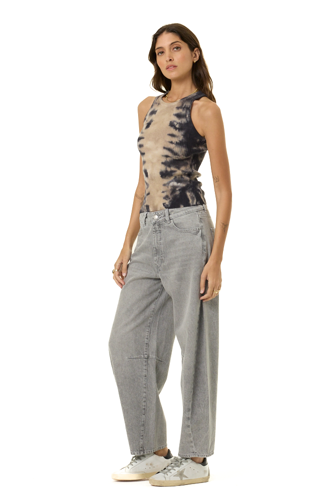 A woman modeling a sleeveless tie-dye top with a beige and black spiral pattern, paired with light gray wide-leg jeans and white sneakers, against a plain white background.