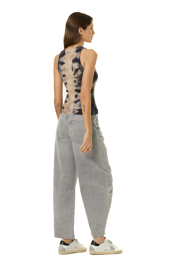 A woman shown from the back wearing a sleeveless tie-dye tank top, loose light gray wide-leg jeans, and white sneakers, photographed against a plain white studio background.