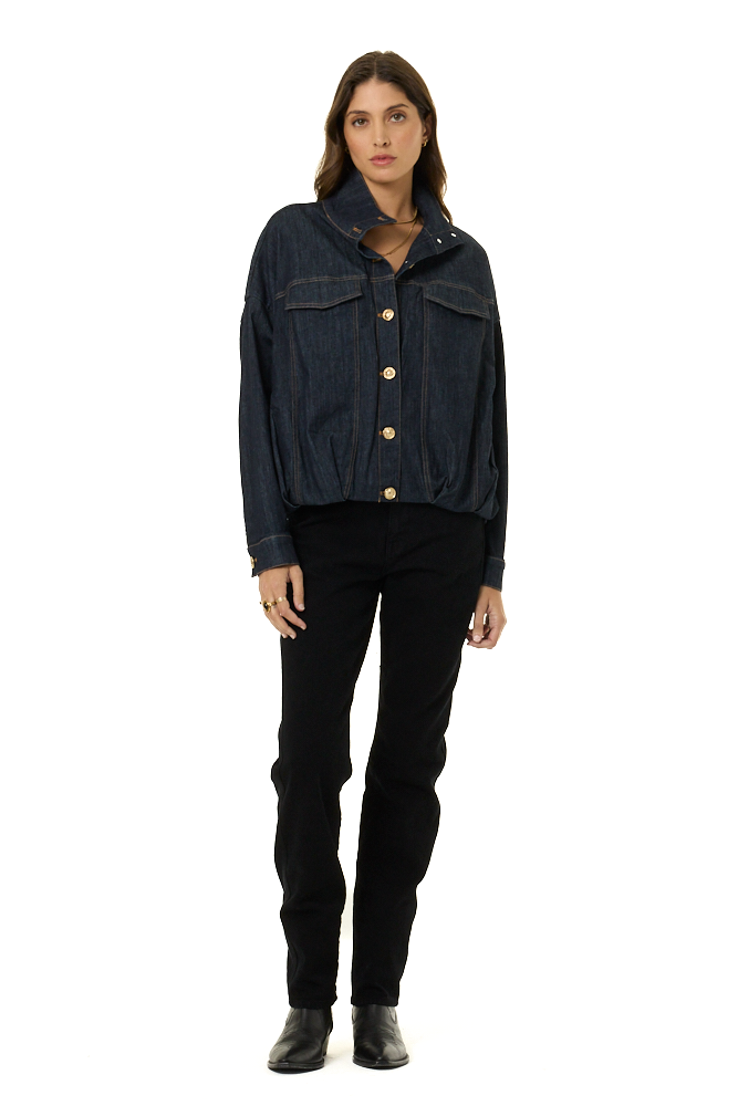 A model wearing a dark indigo denim jacket with gold buttons, paired with black pants and black boots, standing against a solid white background.