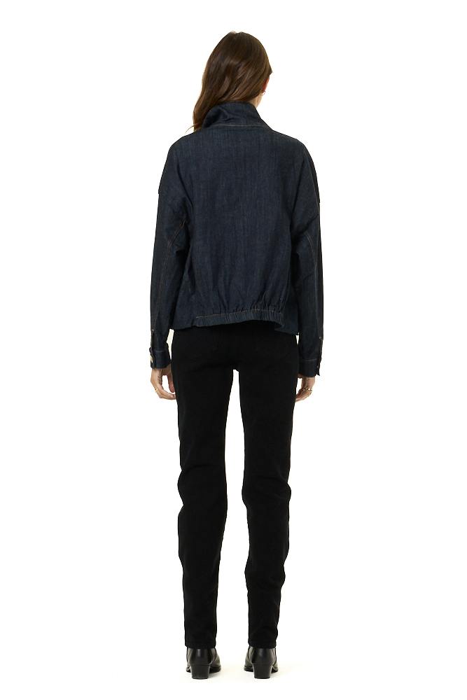 A woman viewed from the back wearing a dark indigo denim jacket and black pants against a plain white background.