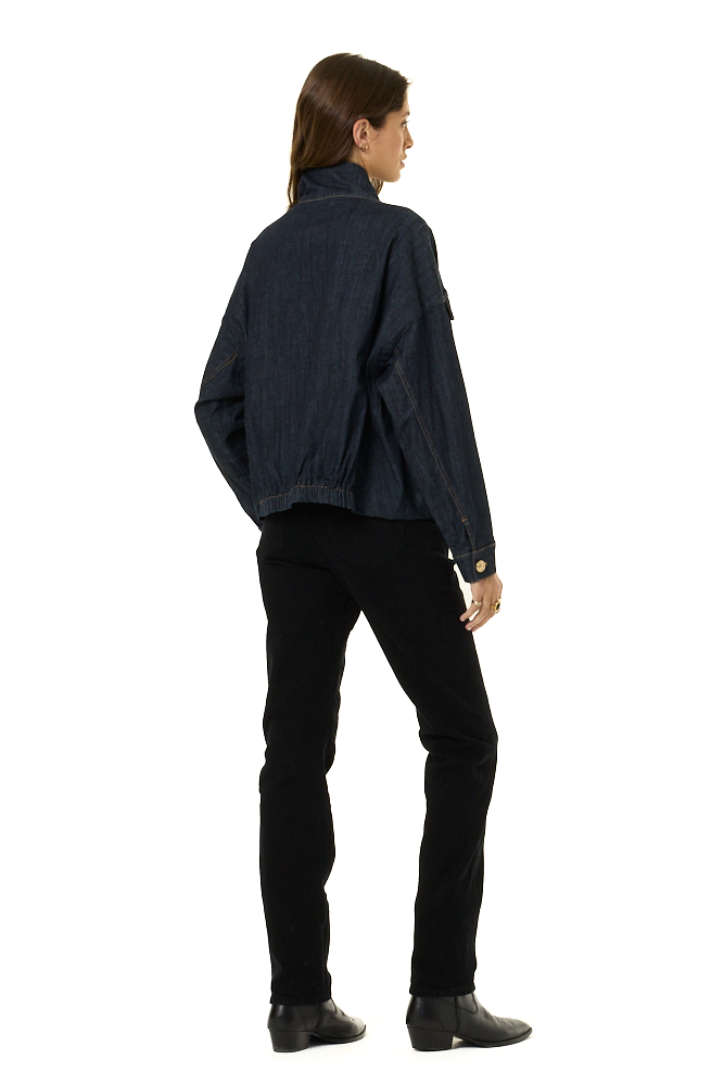 A model shown from the back wearing a dark indigo denim jacket, black pants, and black boots against a plain white background.