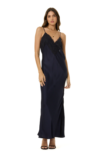A woman modeling a dark navy blue maxi slip dress with thin straps and a ruffled neckline, standing against a plain white background.