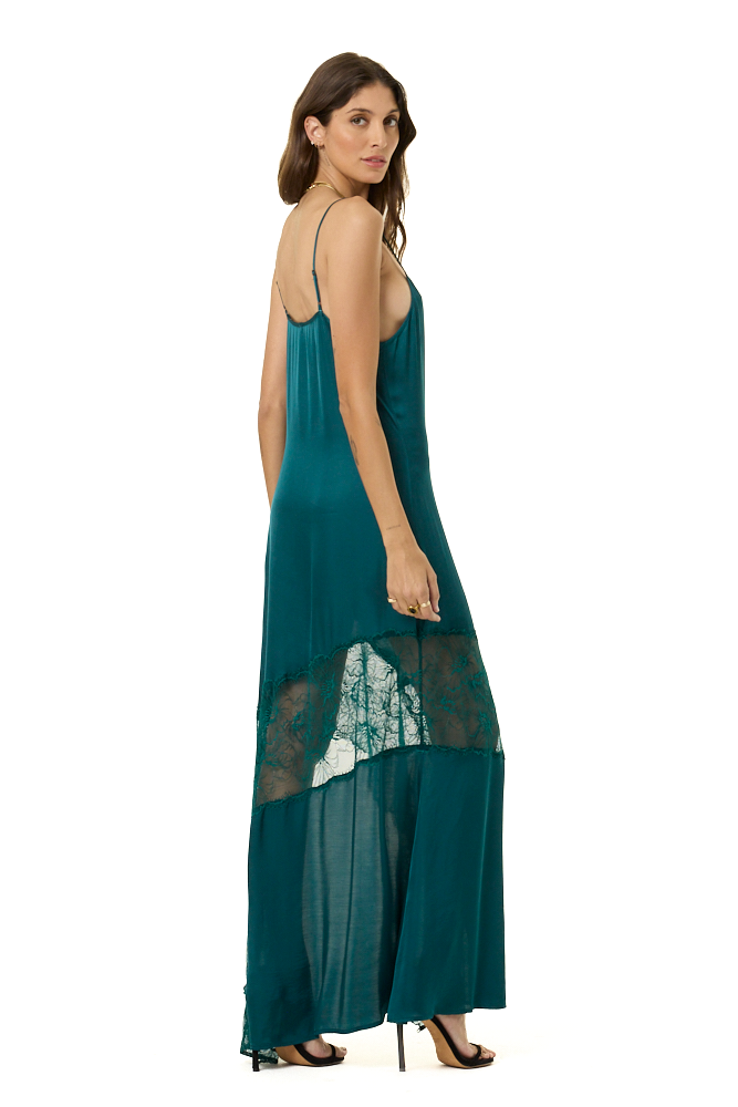 A woman modeling a teal green maxi dress with spaghetti straps, a sheer overlay, and a lace panel near the hem, shown from a side-back angle against a plain white background.