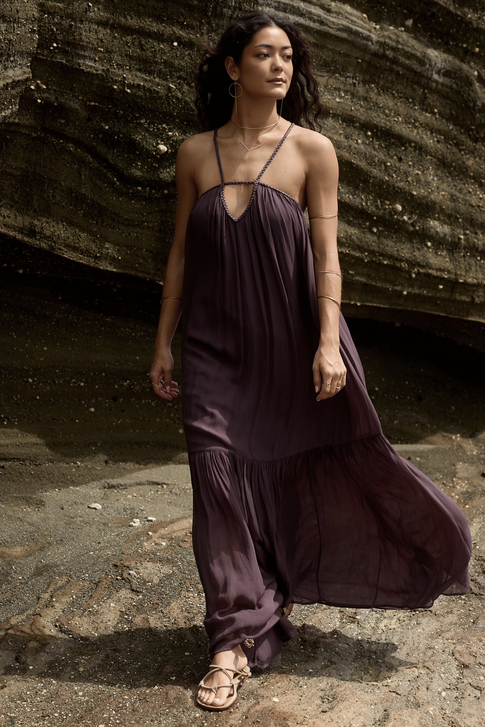 Woman wearing a long, dark purple dress standing against a textured wall.