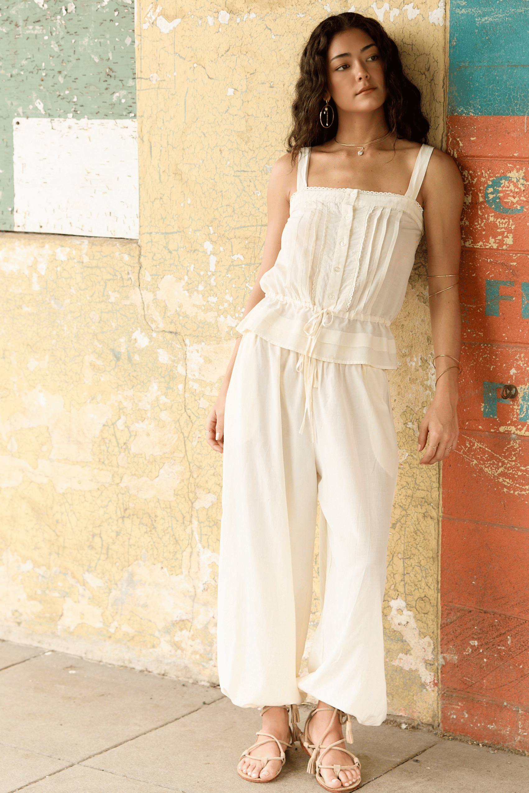 Woman wearing a white pant set standing against a textured wall.