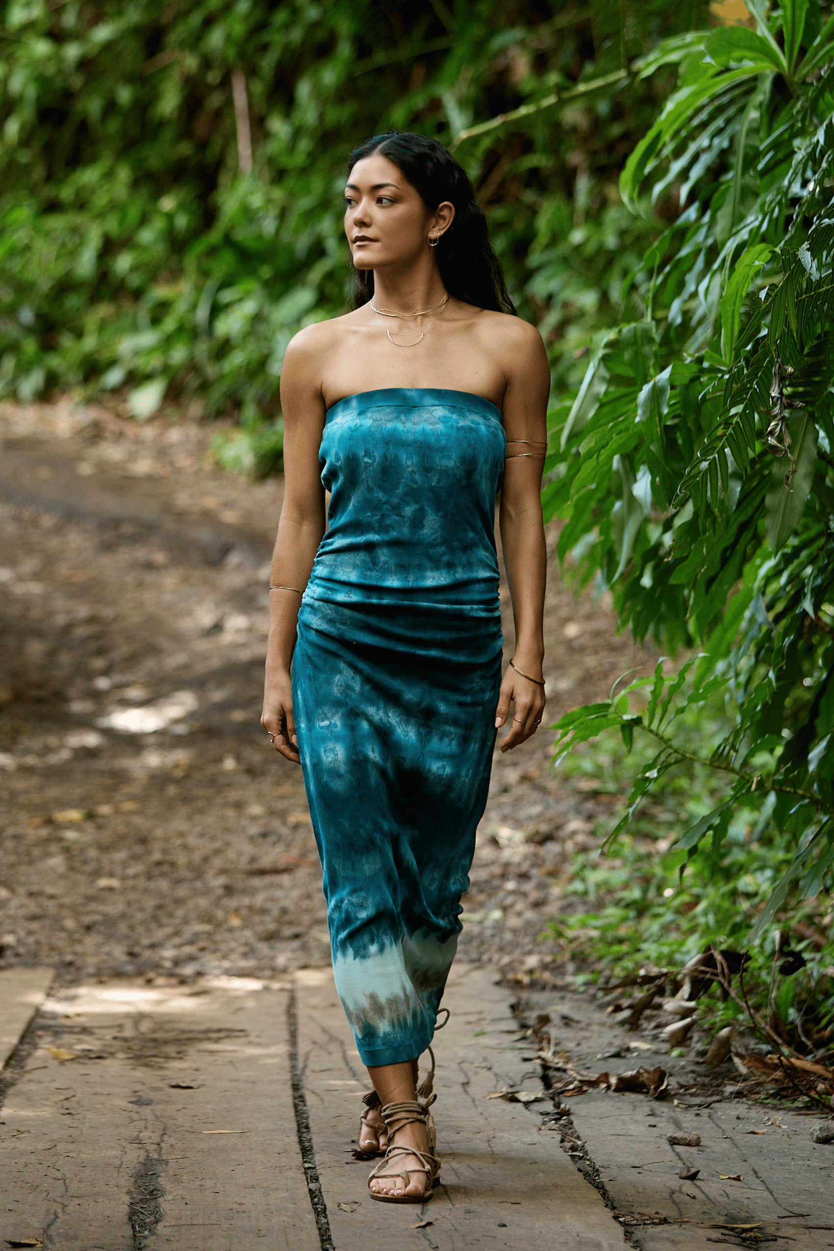 Woman in a blue tie-dye dress walking on a path in a forest