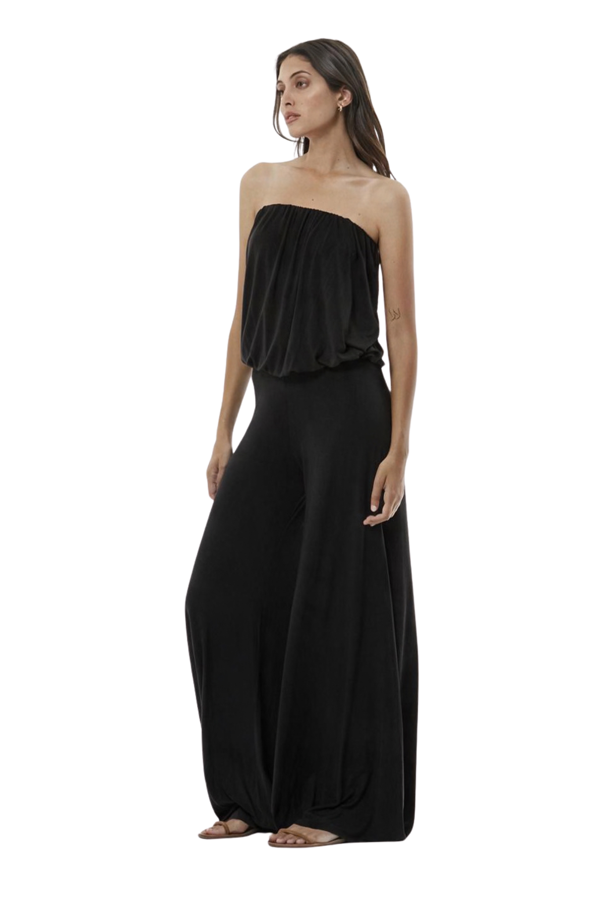 A woman modeling a black strapless jumpsuit with wide legs, photographed against a plain white studio background.