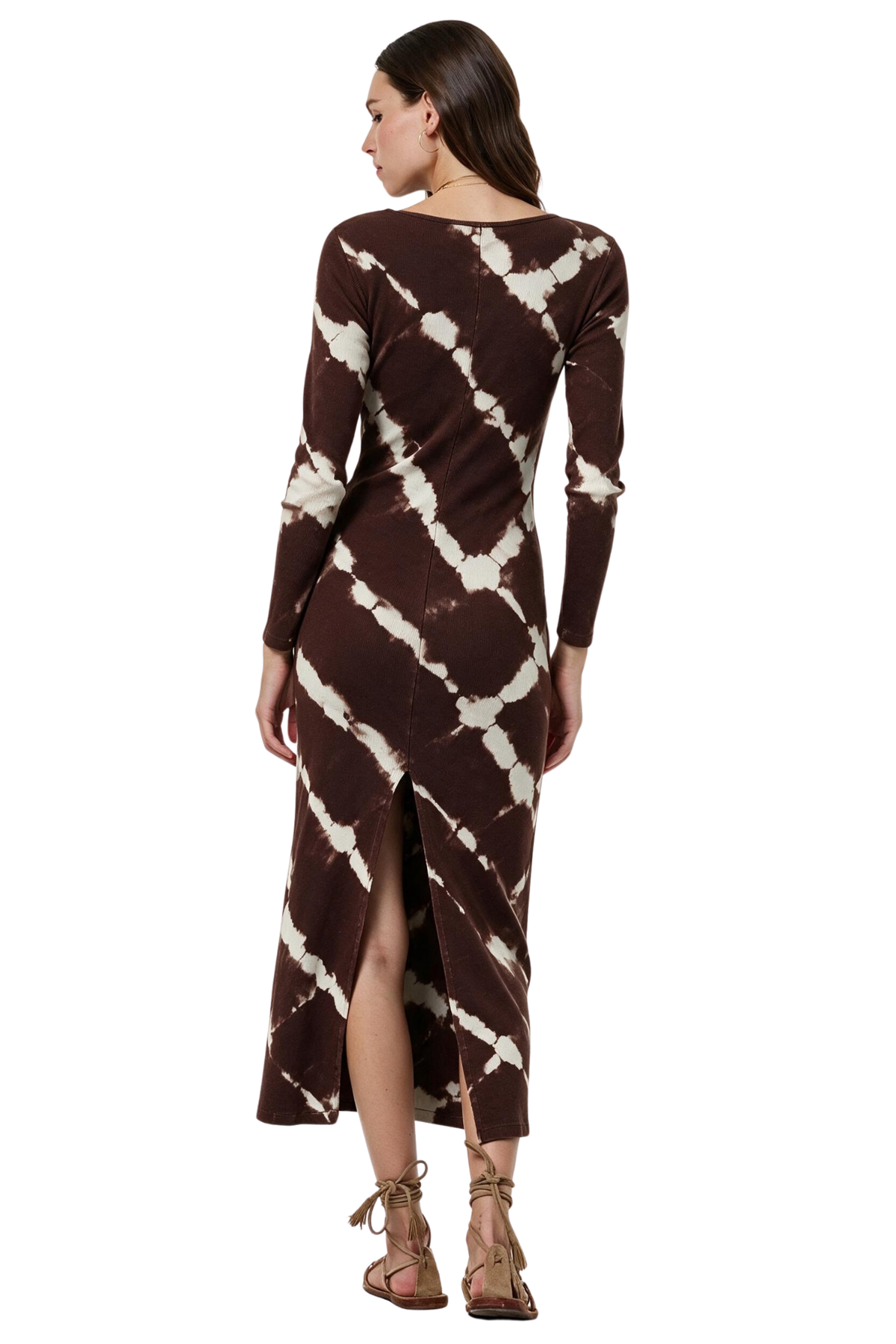 A woman modeling a long-sleeve brown and cream tie-dye maxi dress from the back, featuring a diagonal tie-dye pattern and a front slit, paired with brown lace-up sandals against a white background.