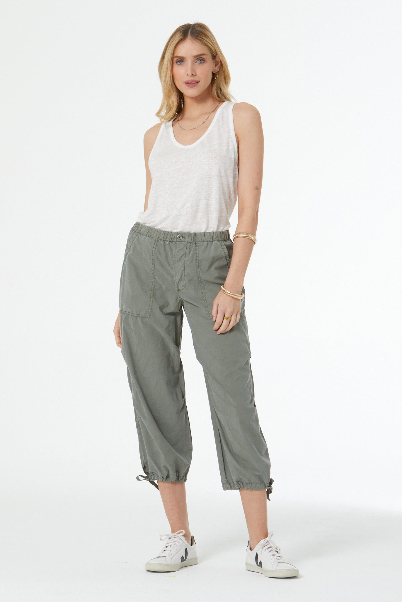 Woman wearing a white sleeveless top and green pants on a white background