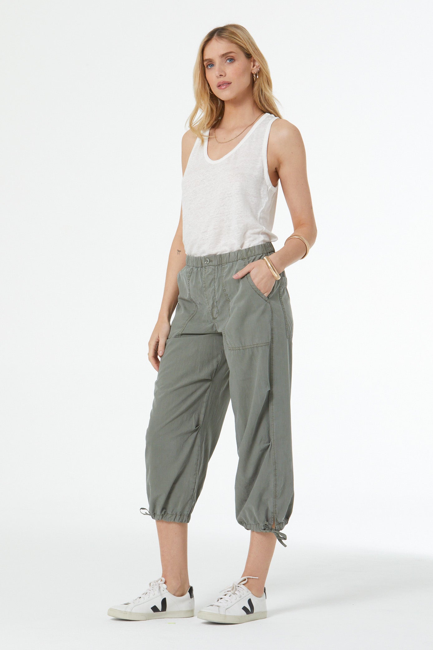 Woman wearing a white sleeveless top and gray pants on a white background