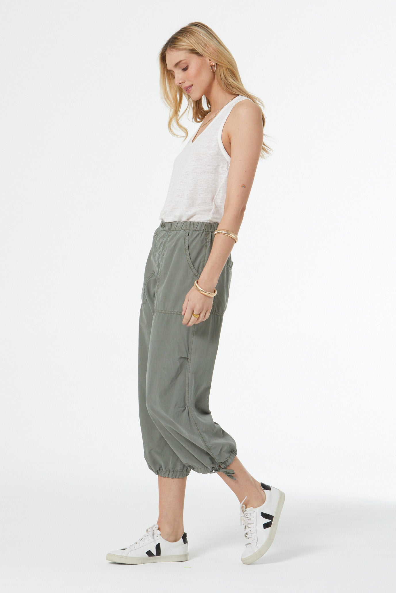 Woman wearing a white sleeveless top and green pants on a white background