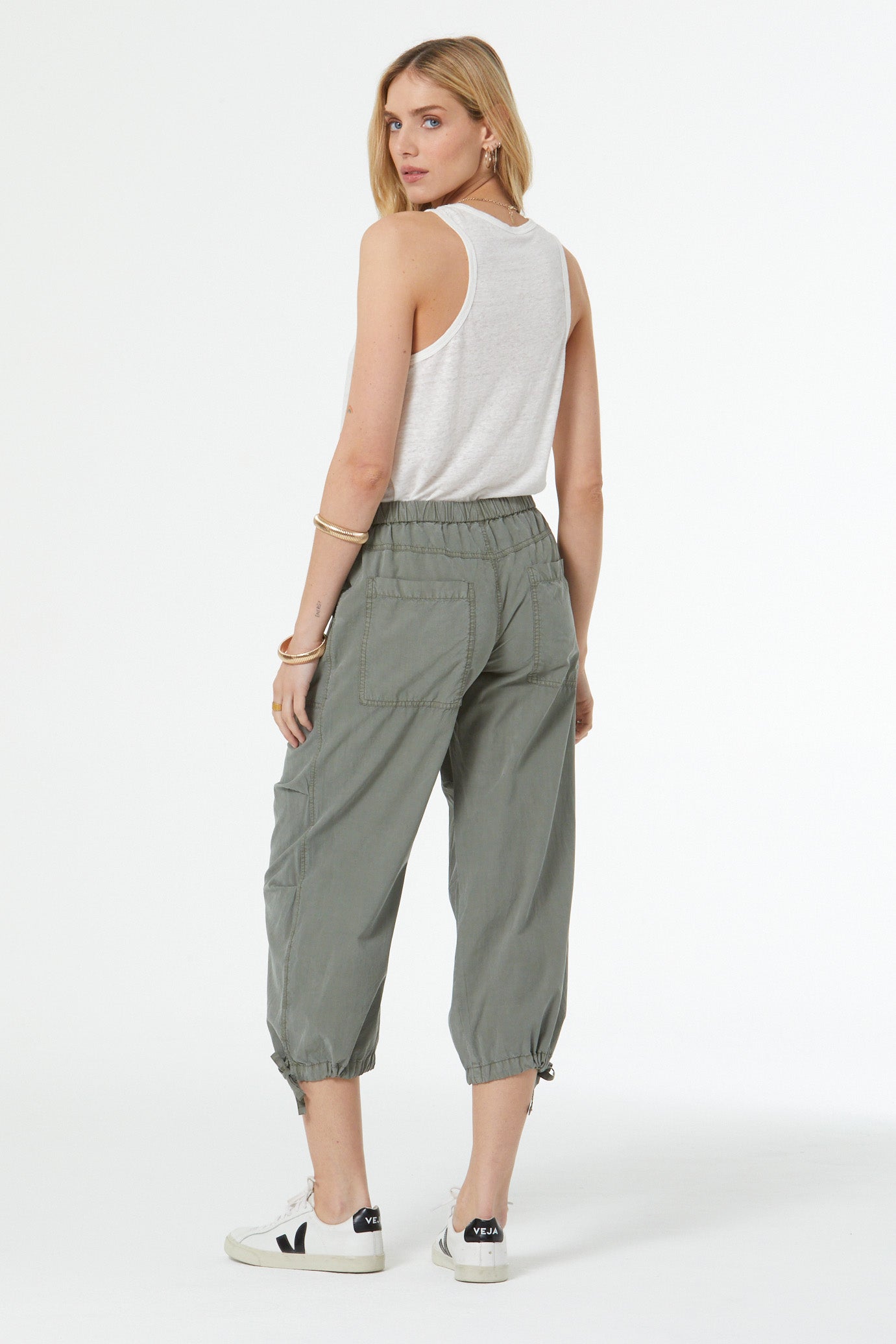 Woman wearing a white sleeveless top and green pants on a white background
