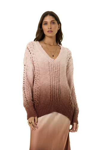 A woman modeling a pink and brown ombre knit sweater with a V-neck and textured openwork sleeves, paired with a satin slip skirt against a white background.
