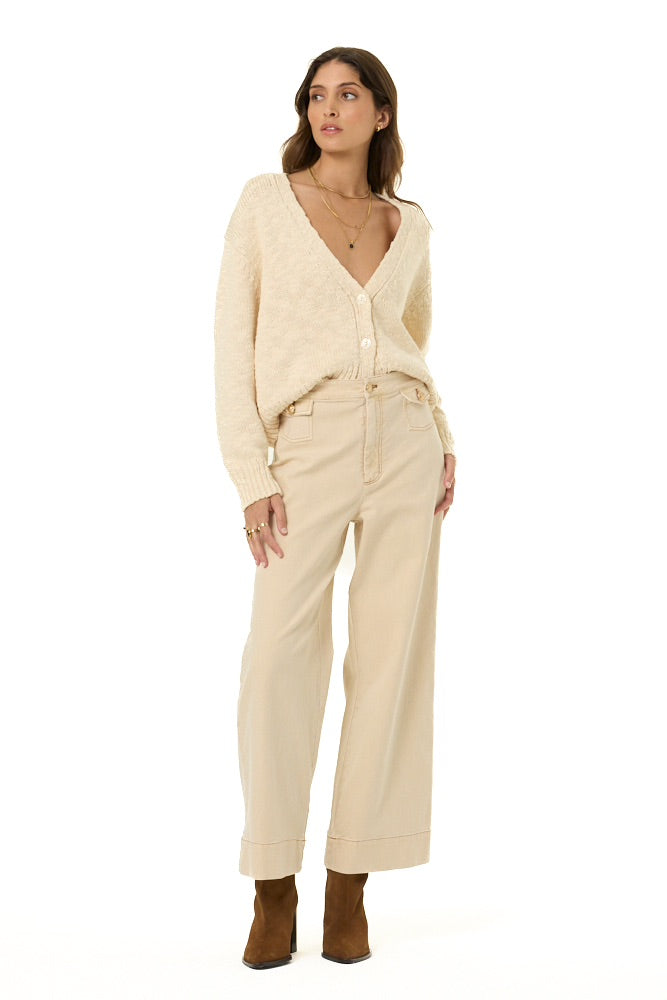 A woman modeling a cream-colored knit cardigan and matching wide-leg trousers, paired with brown ankle boots, against a plain white background.