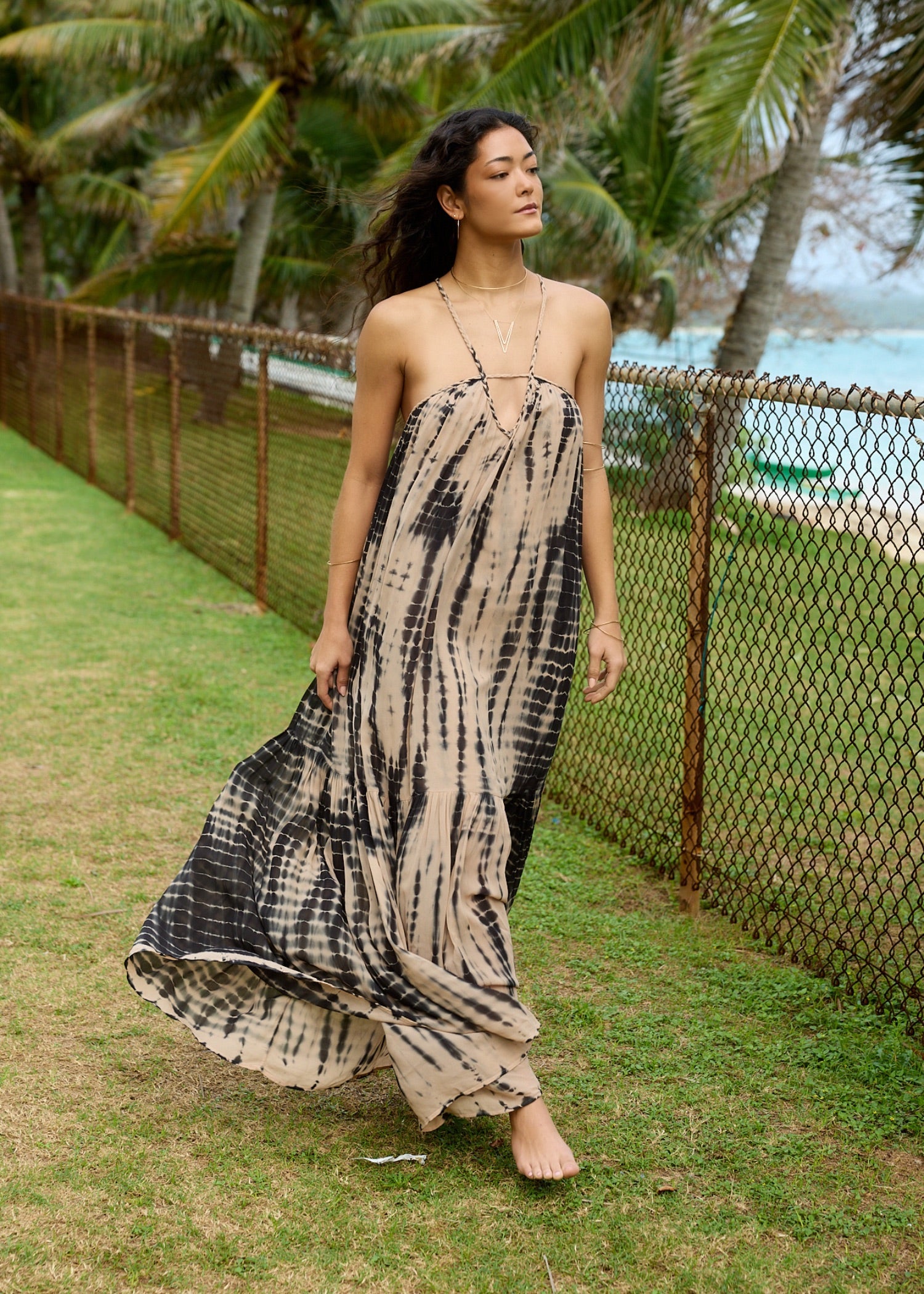 ADA compliant: Shop Seasonal Fabrics collection. Woman wearing a chiffon flowy tan and black dress in a grassy scene with the ocean in the background