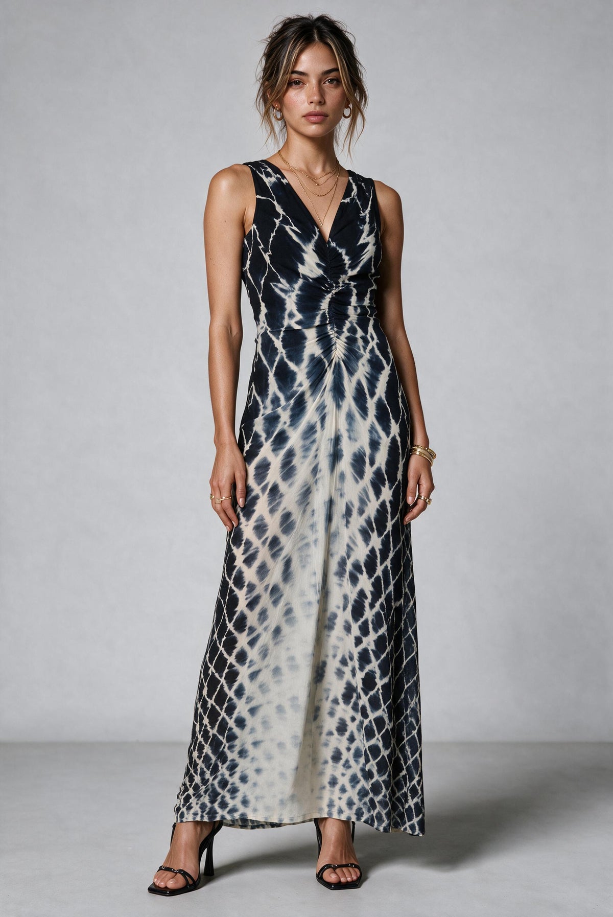 A woman modeling a sleeveless maxi dress with a black and off-white tie-dye pattern, standing against a neutral gray studio background.
