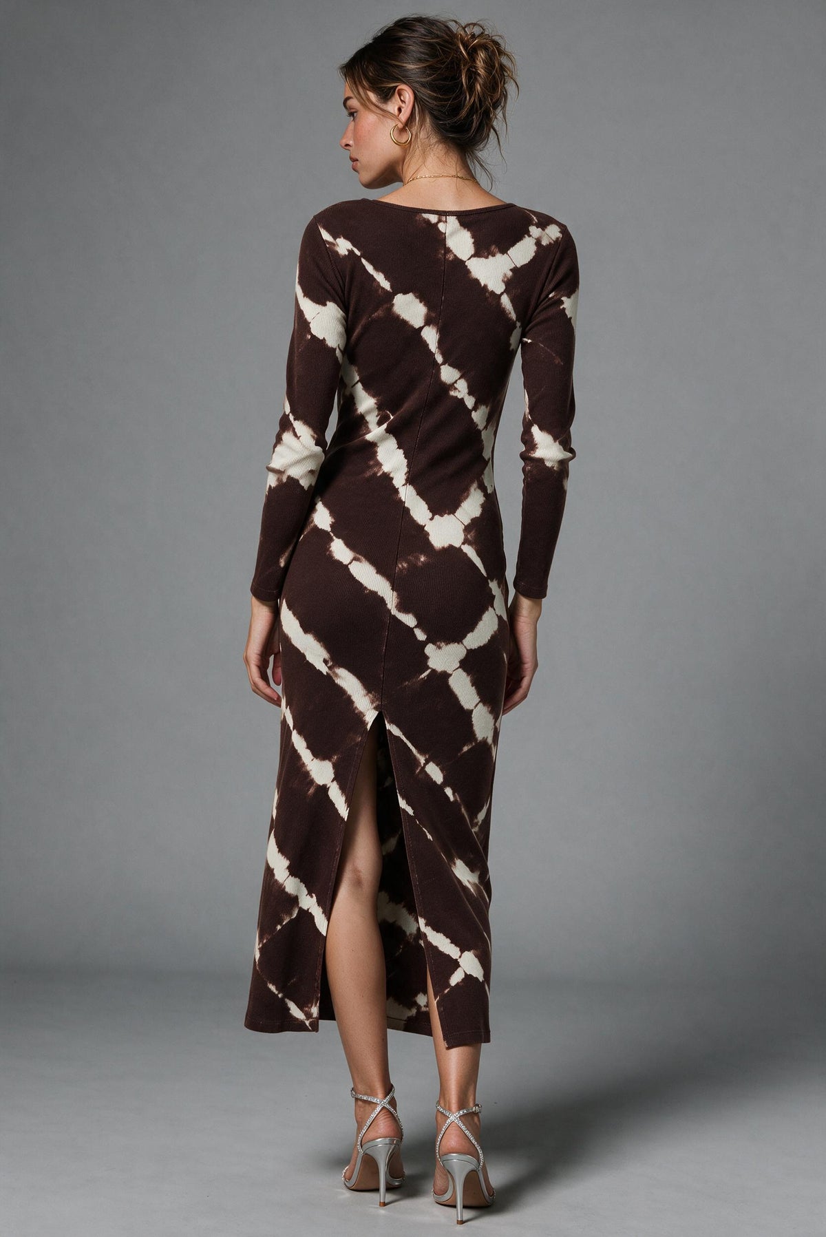 A woman modeling a long-sleeve midi dress with a brown and cream tie-dye pattern, shown from the back against a neutral gray studio background.