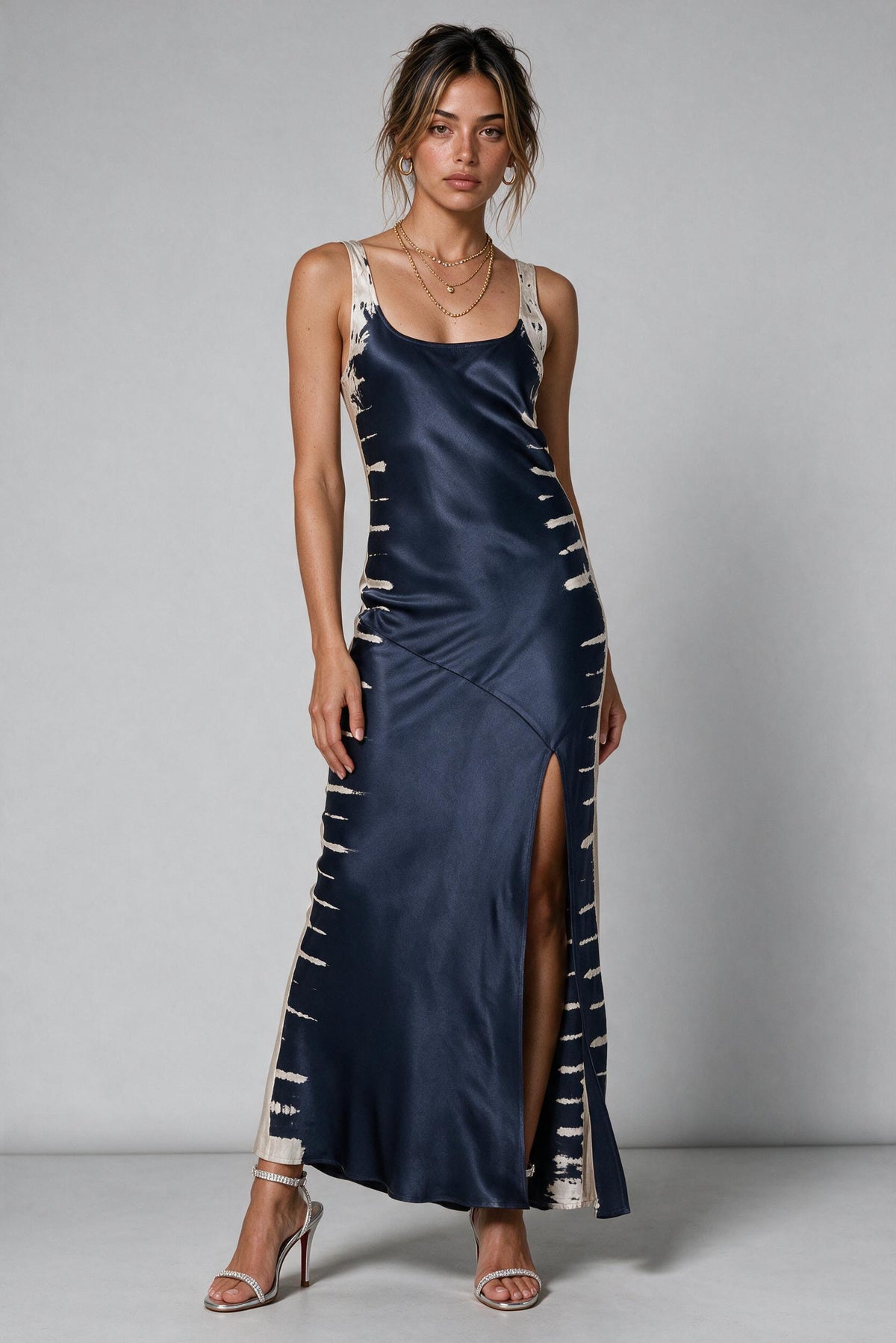 Woman wearing a bias cut slip satin dress with a high front slit in a blueish gray tie-dye print.