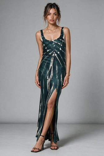 A woman modeling a sleeveless dark green maxi dress with a white tie-dye pattern, featuring a high thigh slit and a draped, gathered neckline, set against a plain gray studio background.