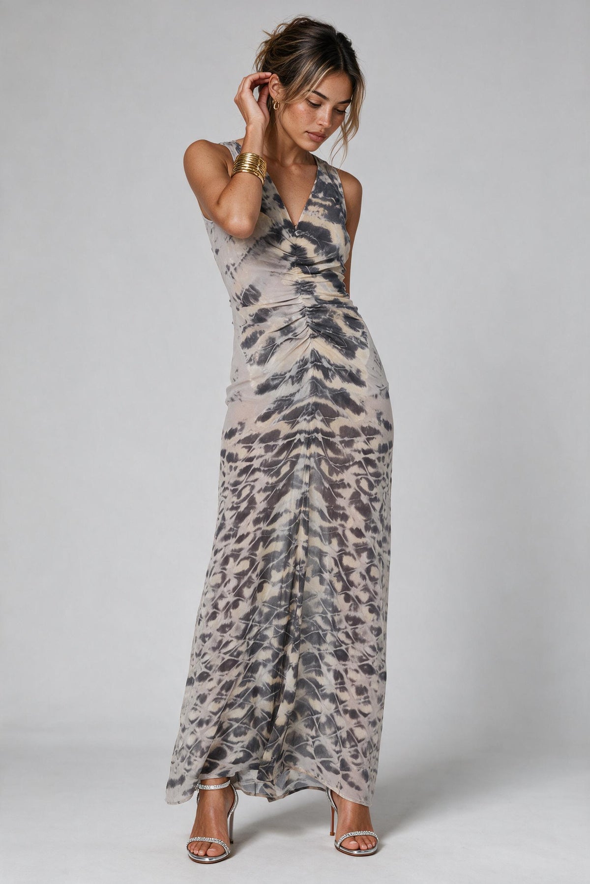 A woman modeling a sleeveless, floor-length dress with an abstract gray, black, and beige animal-inspired print against a light gray studio background.