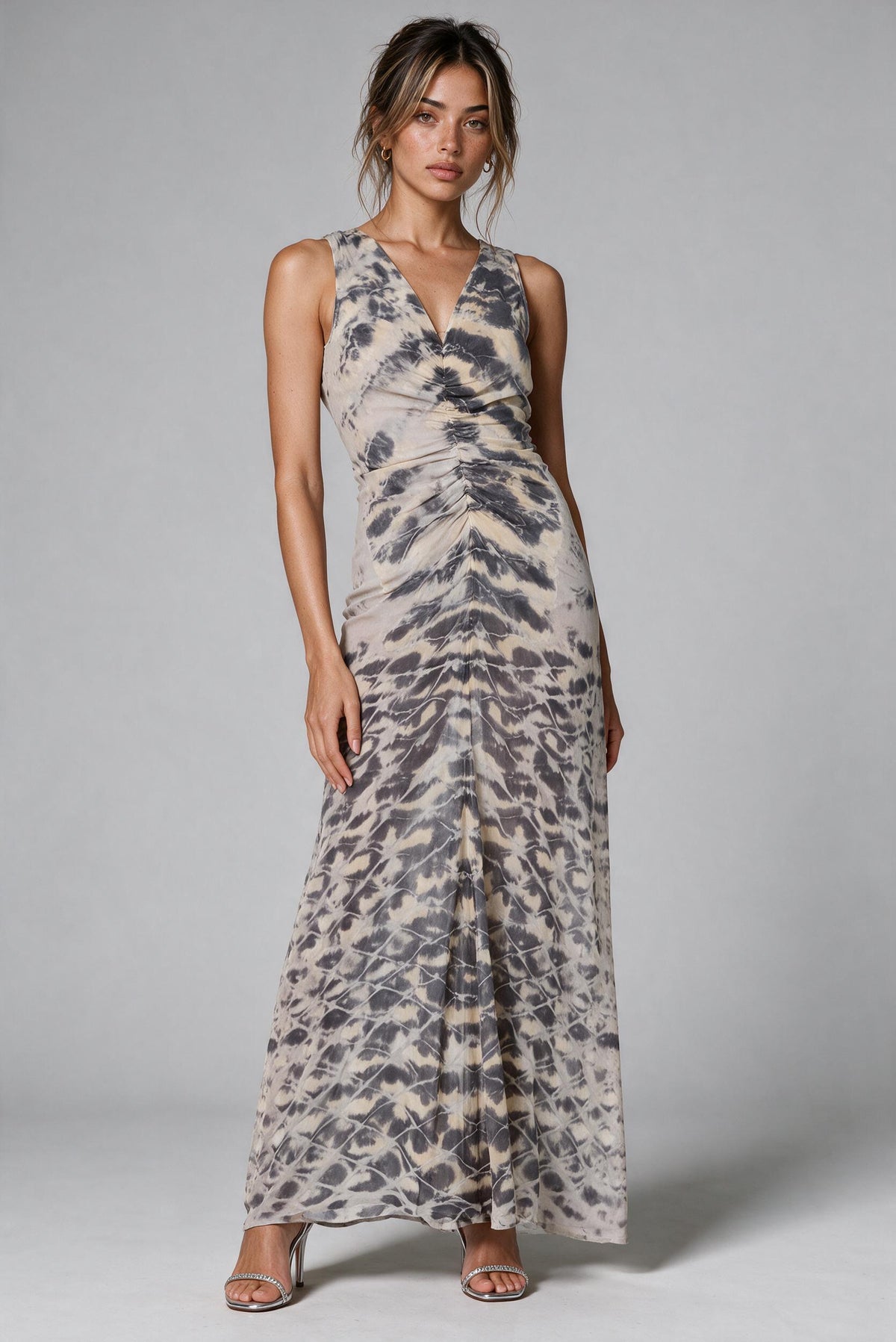 A woman modeling a sleeveless, V-neck maxi dress with a gray and beige abstract animal print, standing against a neutral gray studio background.
