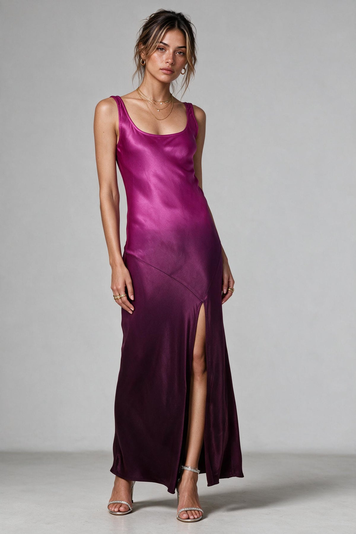 A woman modeling a floor-length satin slip dress in a rich magenta-purple color, shown from the back against a neutral gray studio background.