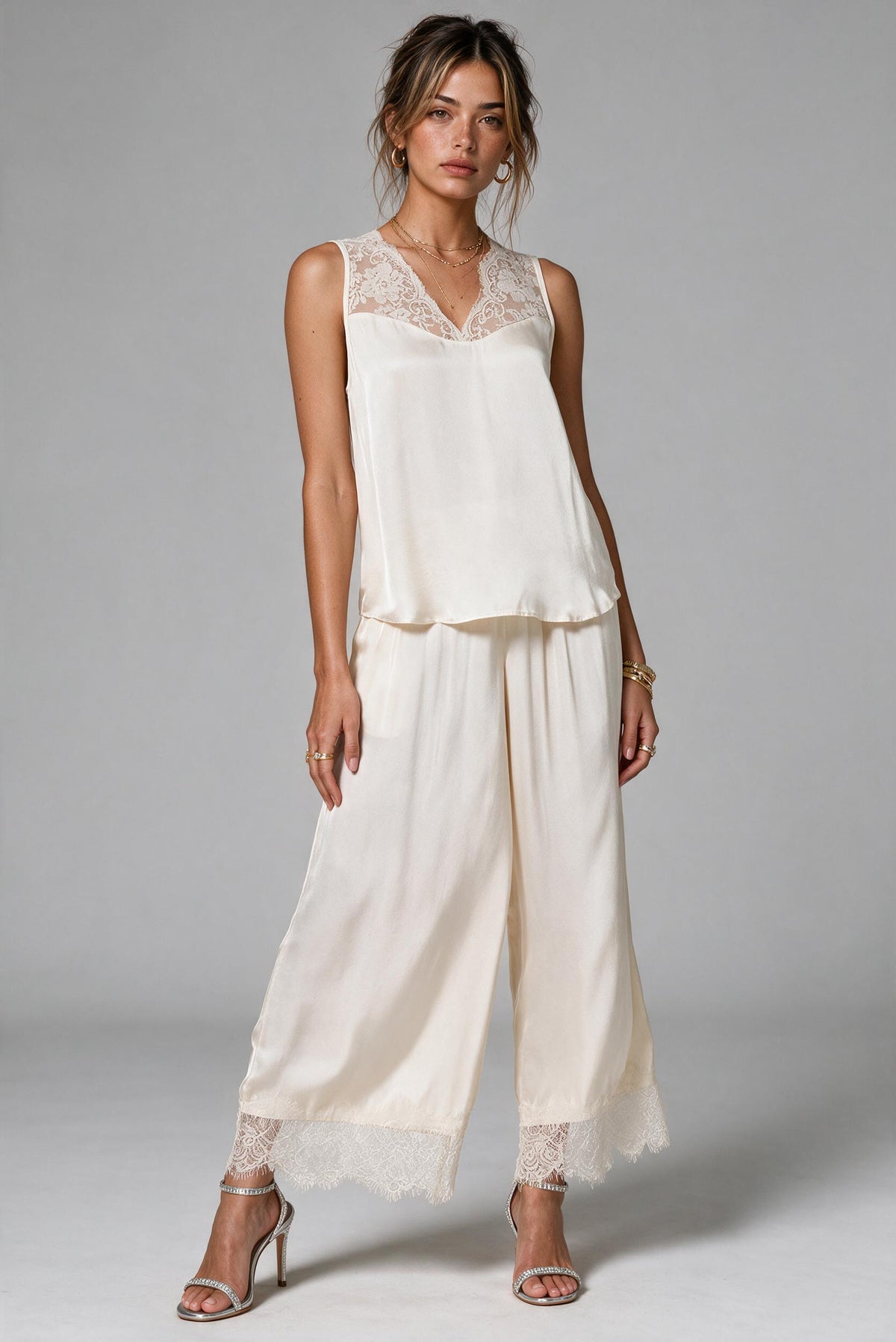 A woman wearing a matching cream satin outfit with lace-trimmed wide-leg pants and metallic silver heels.