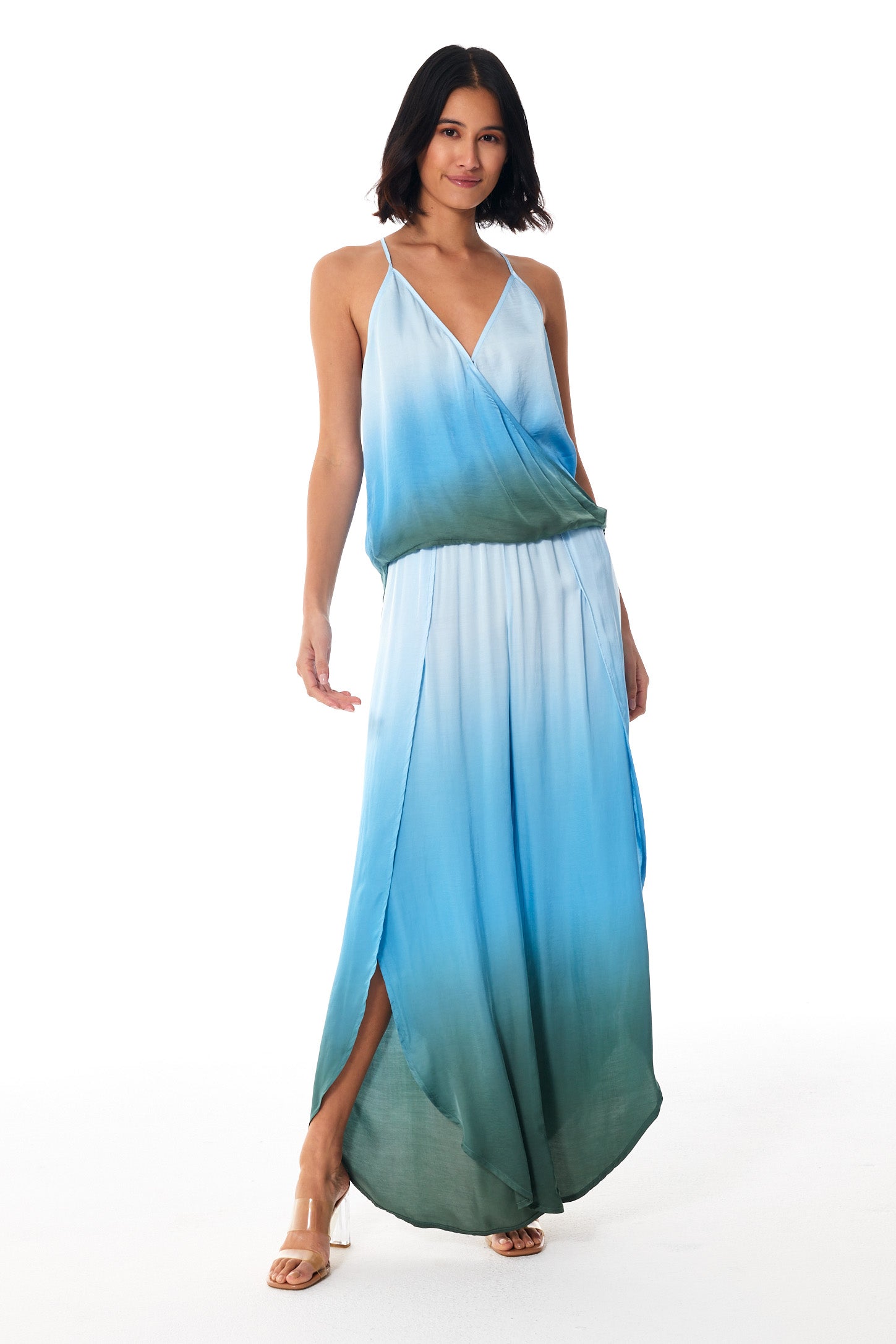 A woman modeling a sleeveless wrap-style maxi dress with a gradient ombre design transitioning from sky blue at the top to deep teal at the bottom, set against a plain white studio background.