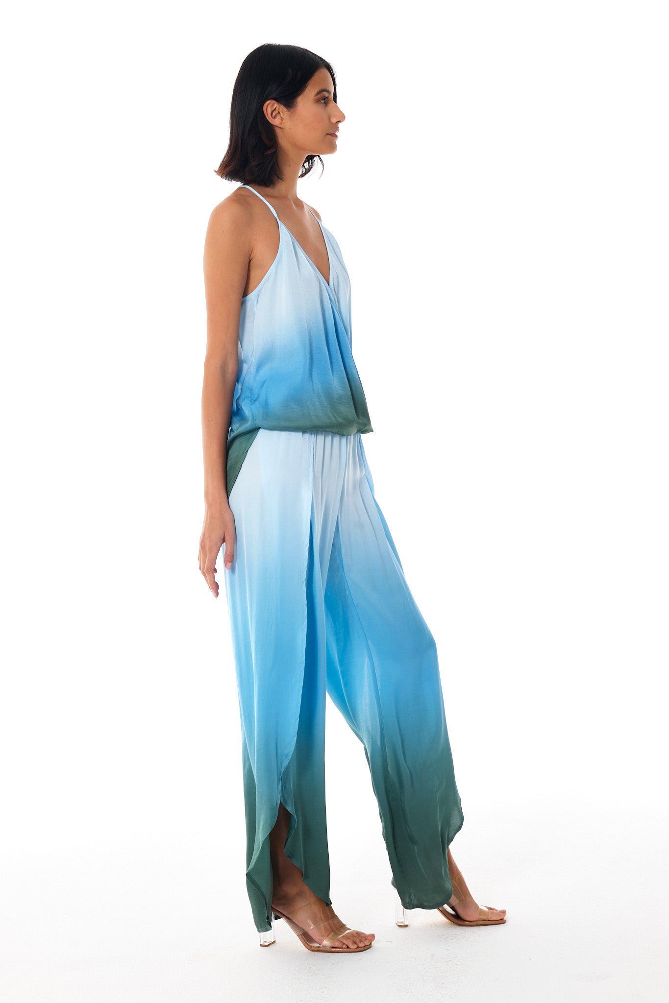 A woman modeling a sleeveless two-piece jumpsuit with a blue and green ombre gradient, shown from a side profile against a white studio background.