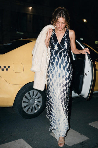 Woman getting out of a taxi cab wearing a black and white links printed dress with a fur coat draped over er shoulder.